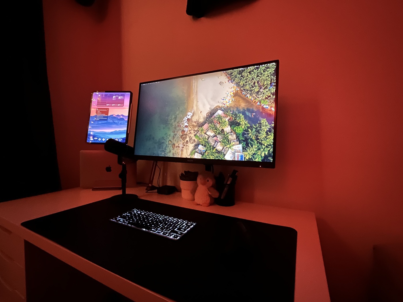 Desk setup with monitor, tablet, laptop, microphone, keyboard, mouse, and desk mat